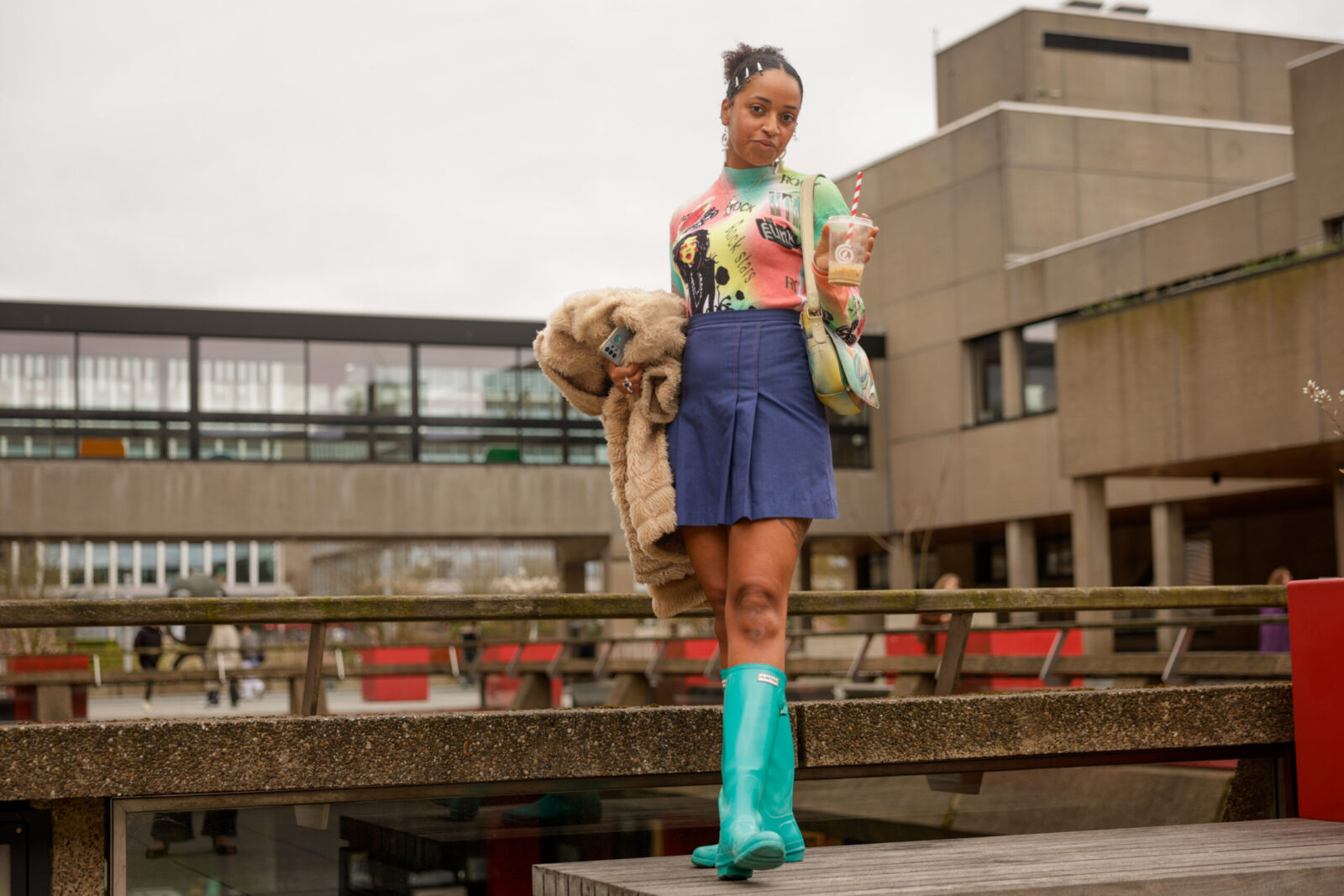 Benita draagt een roze, groen en geel shirt, een donkerblauwe rok en fel turquoise regenlaarzen
