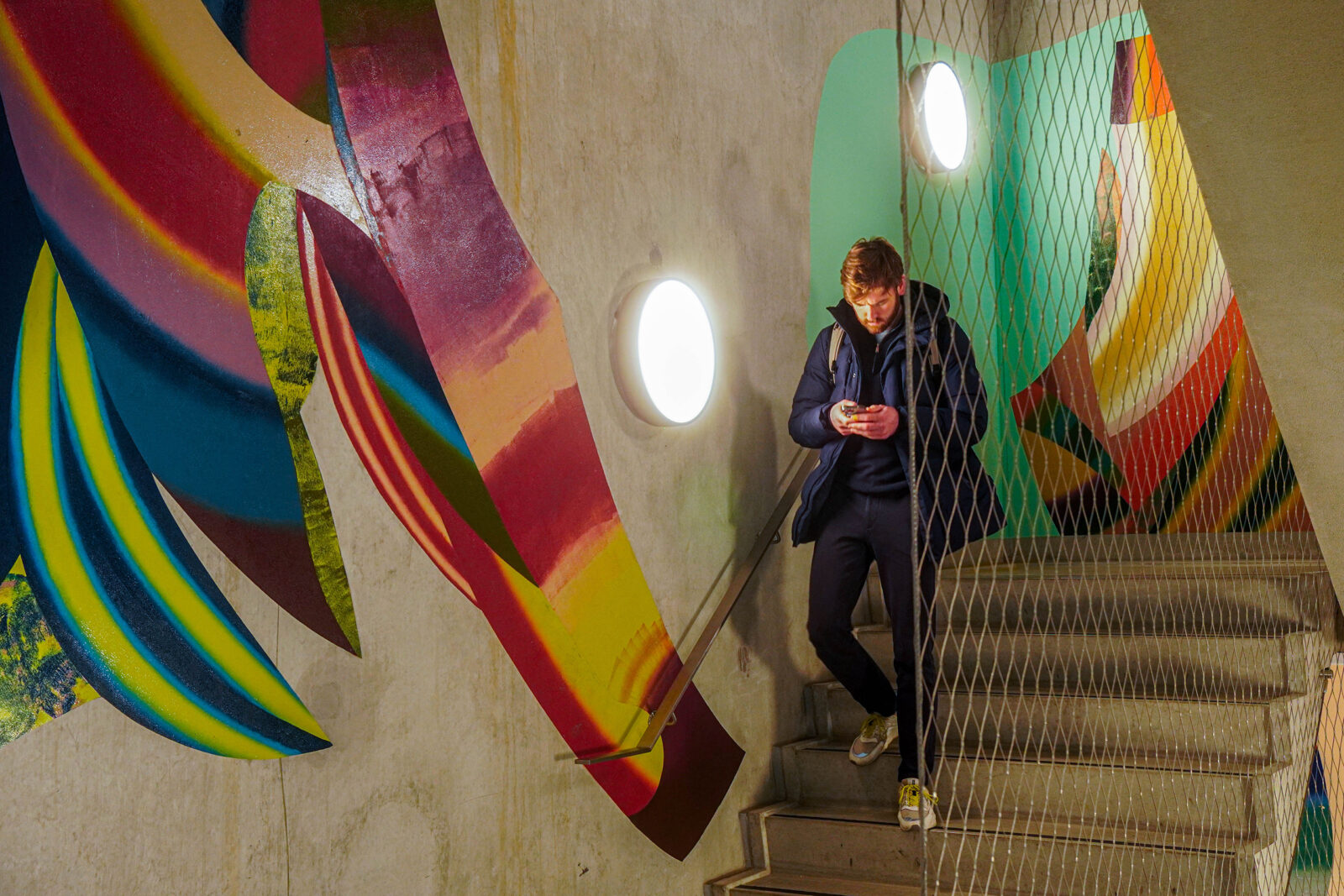 A student walks down the stairs past the colourful mural.