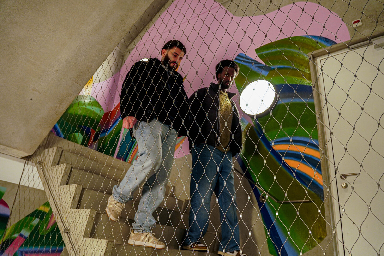 Two students walk down the stairs past the colourful mural.