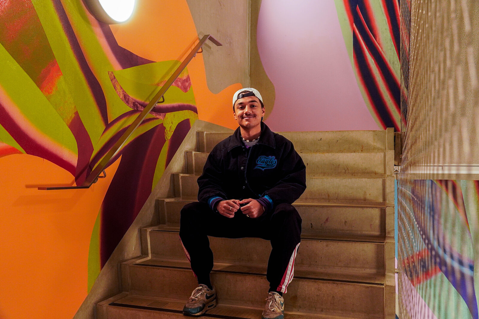 Student Roman is sitting on the steps in front of the mural in the Langeveld building.