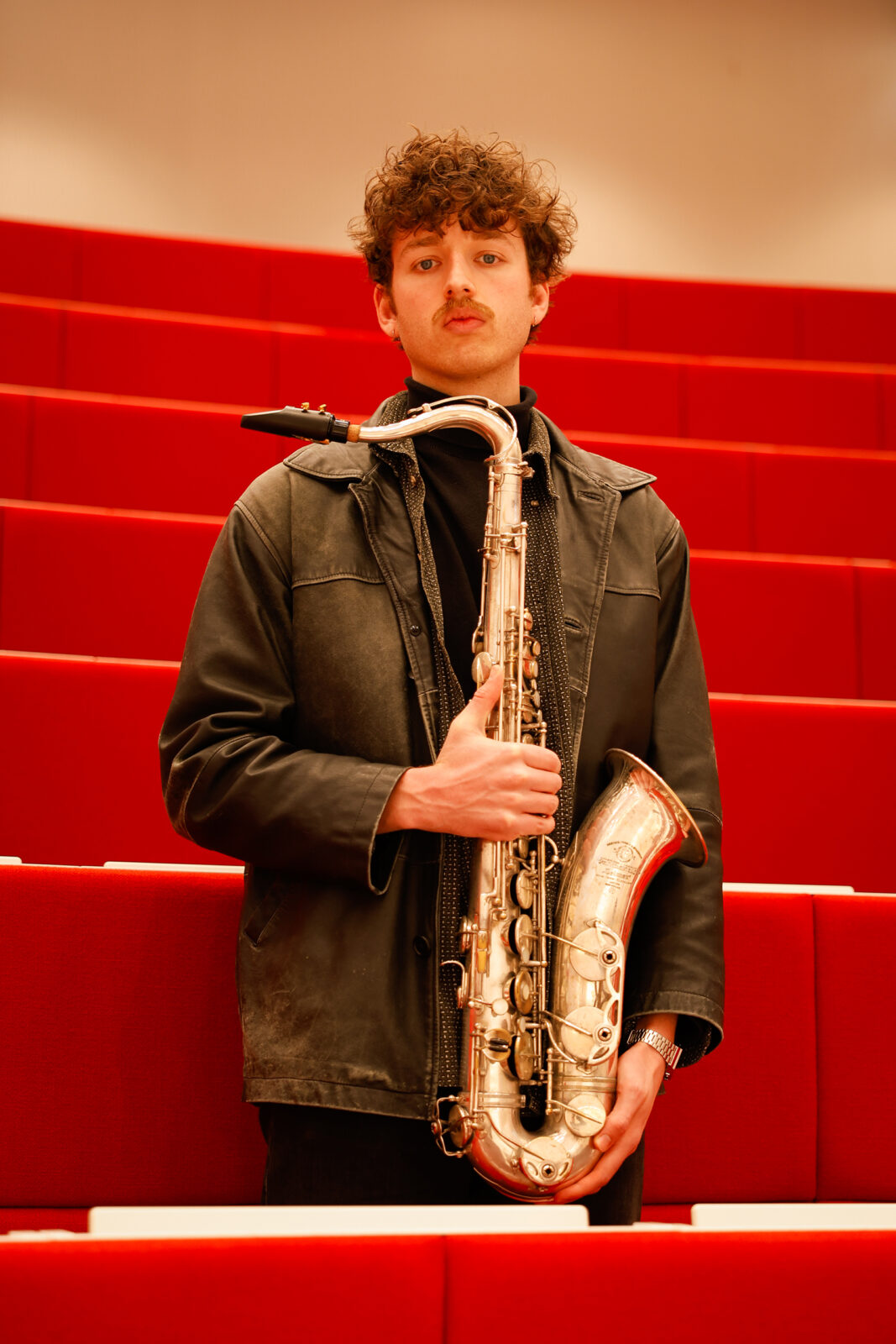 Daan Kluwer met saxofoon in een Erasmus MC collegezaal.