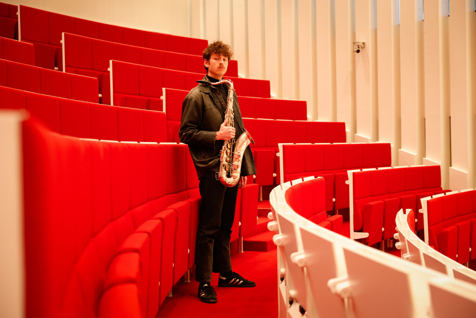 Daan Kluwer met saxofoon tussen de collegebanken in een Erasmus MC collegezaal.