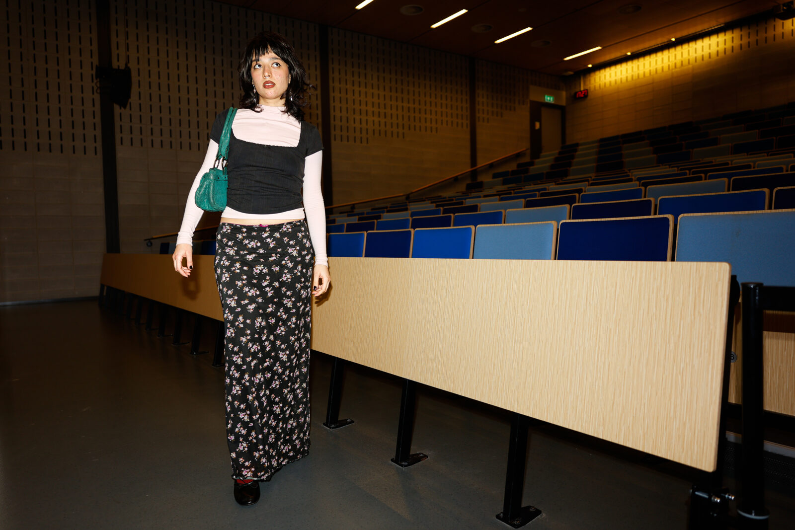 Narmin draagt een rok met roze en paarse bloemetjes, een roze coltrui met daar een zwarte kanten top overheen